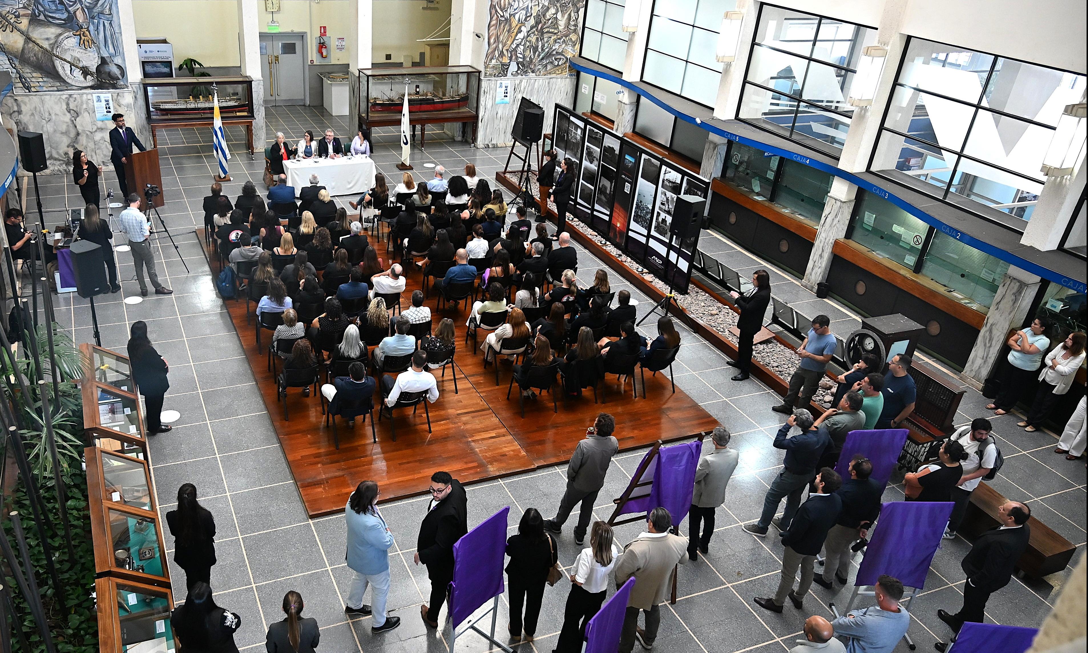 Sala con sillas y personas sentadas con expositores en mesa al frente